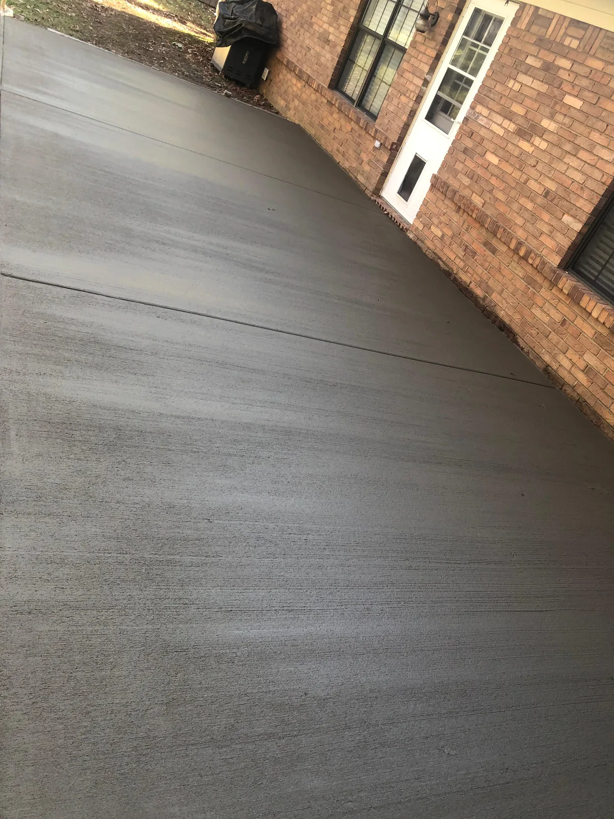 Fresh broom-finished concrete poured along a brick home
