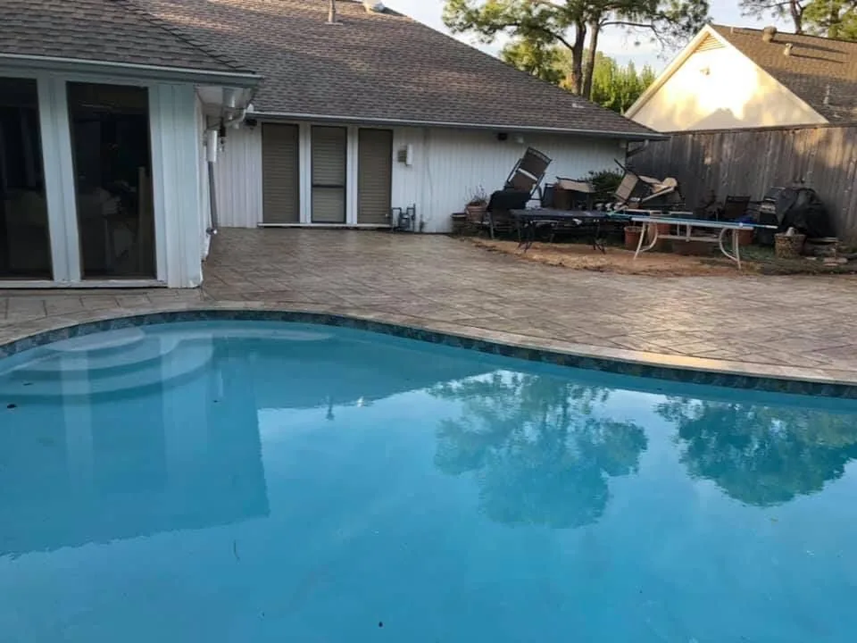 Wide stamped concrete pool deck behind a home