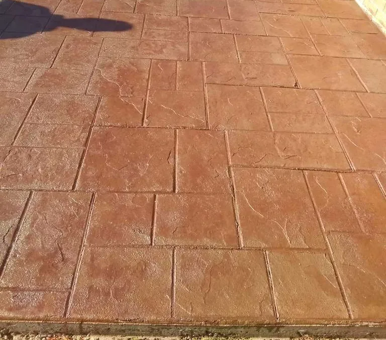 Red stamped concrete walkway curving through a lawn
