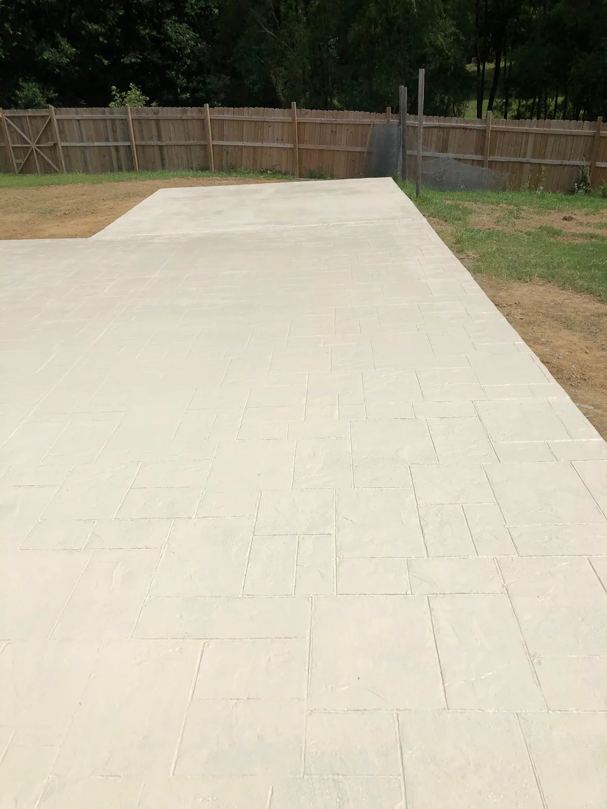 Light stamped concrete patio in a fenced backyard